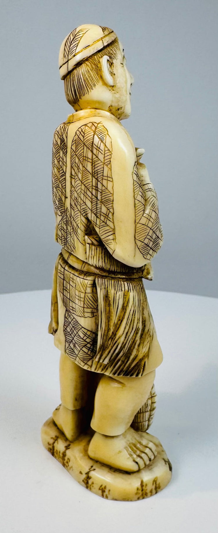Side view of a Japanese carved fisherman standing barefoot on an oval base