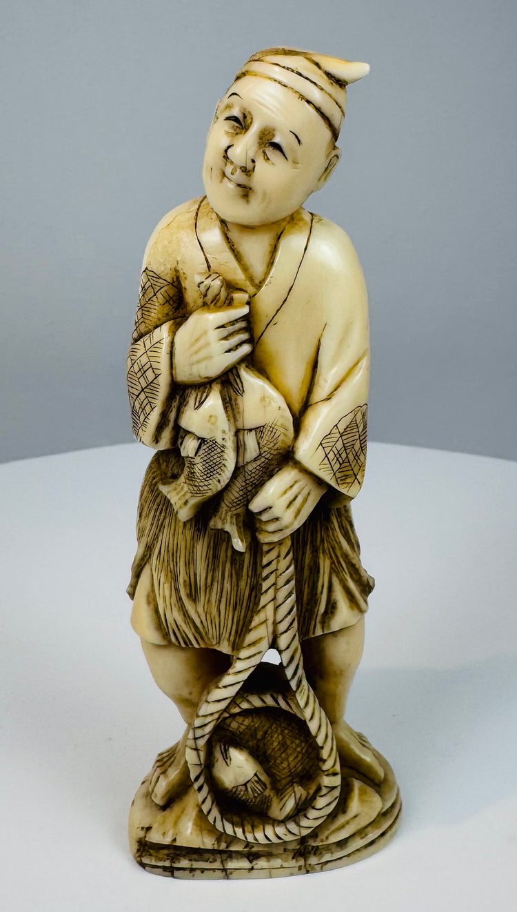 Front view of a Meiji–Taishō Japanese fisherman carving holding his catch