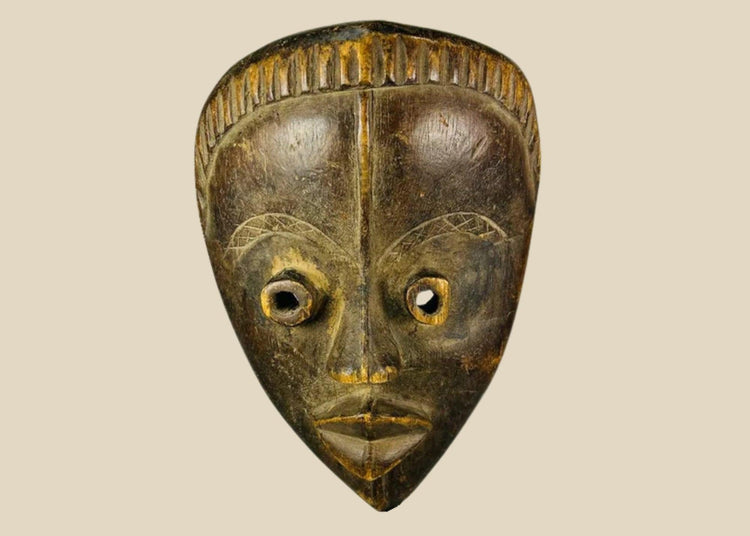 Antique Baule tribal mask from Ivory Coast, early 20th century, hand-carved wood with natural patina, oval face, almond-shaped eyes, and stylized features displayed on a stand.