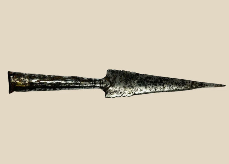 Forged iron spearhead from Europe, Iron Age to Early Medieval period (circa 1st millennium CE), featuring a scalloped-edge blade, socketed base, and historic mixed-metal brazed repair. Natural patina and surface texture reflect centuries of use, craftsmanship, and cultural significance as both a functional weapon and symbol of status.