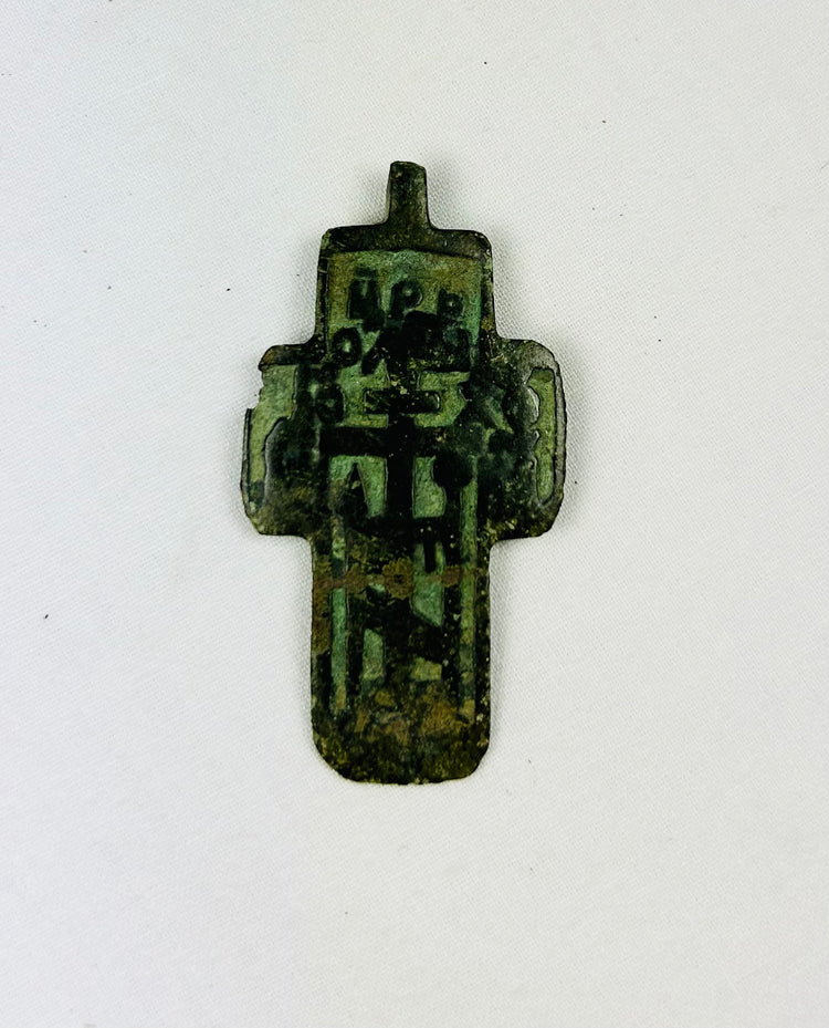 Small Russian Orthodox devotional cross-plaquette from the Old Believer tradition, cast in copper-alloy with champlevé green enamel remnants, blocky Cyrillic inscription panels, and deep olive patina, circa 1780–1820.