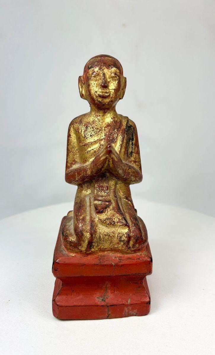 Front view of Southeast Asian gilt-lacquered Buddhist monk statue, kneeling in prayer with gold leaf and red lacquer finish.