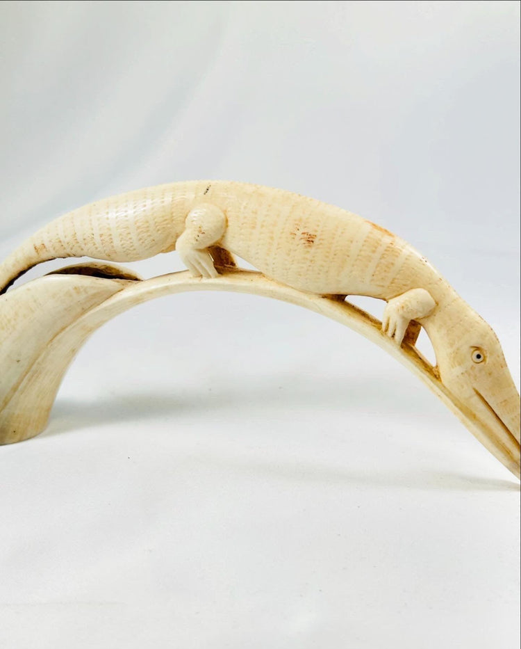 Close-up of early 20th-century African hippopotamus tooth carving depicting a crocodile motif with detailed scales, traditional tribal ivory artwork on white background.