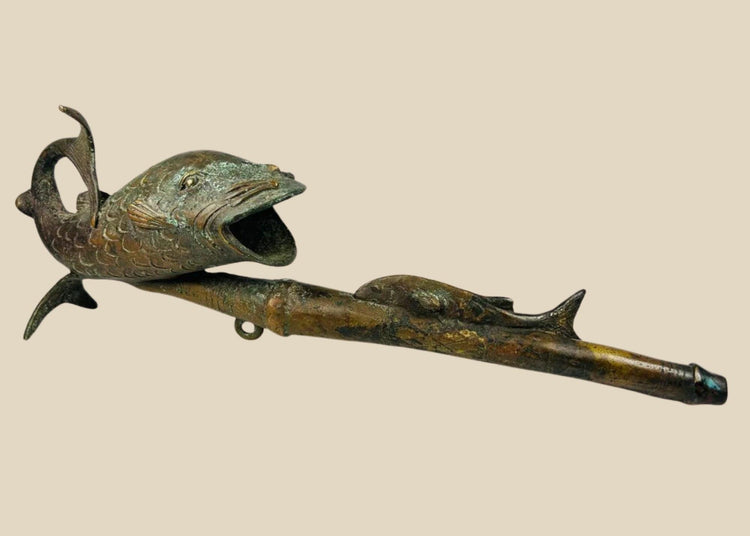 Antique Cameroonian bronze pipe in the form of a fish, early to mid 20th century, cast with detailed scales and curved tail, symbolic of fertility and abundance, shown against a white background.