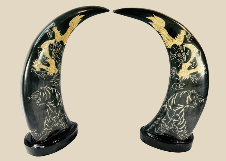Mid–late 20th-century East Asian polished water buffalo horn sculptures etched and painted in gold with celestial dragons and prowling tigers amidst clouds, mounted on black lacquered bases, mirrored composition, circa 1960–1980.