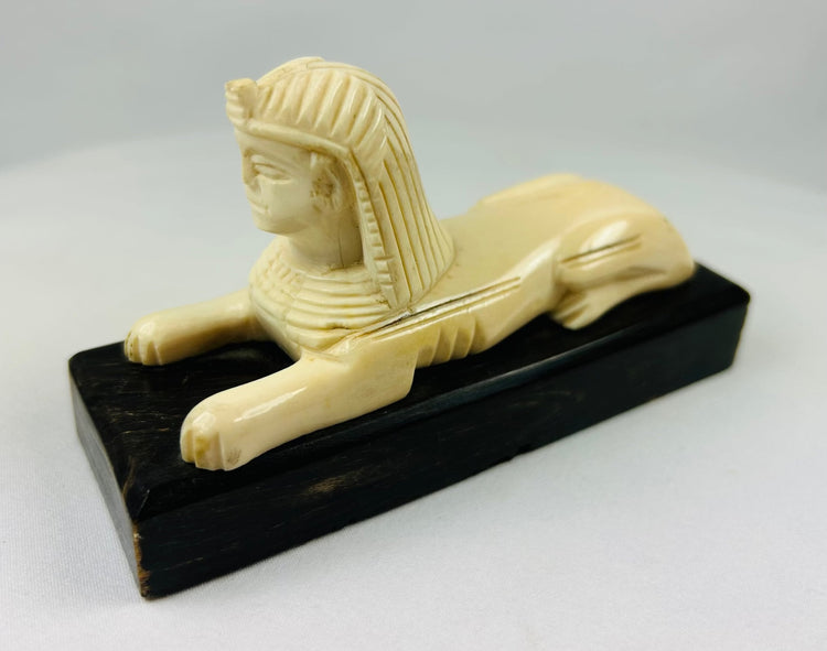 Early 20th century carved sphinx figure inspired by ancient Egyptian art, mounted on black wooden base