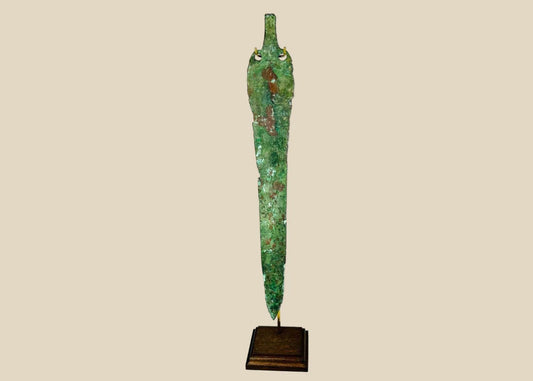 Ancient Bronze Age blade from the Caspian region, circa 2000–1000 BCE, with tapered elongated form, two perforations near the hilt, and rich green patina, mounted on a custom stand.
