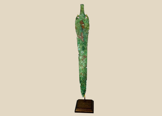 Ancient Bronze Age blade from the Caspian region, circa 2000–1000 BCE, with tapered elongated form, two perforations near the hilt, and rich green patina, mounted on a custom stand.