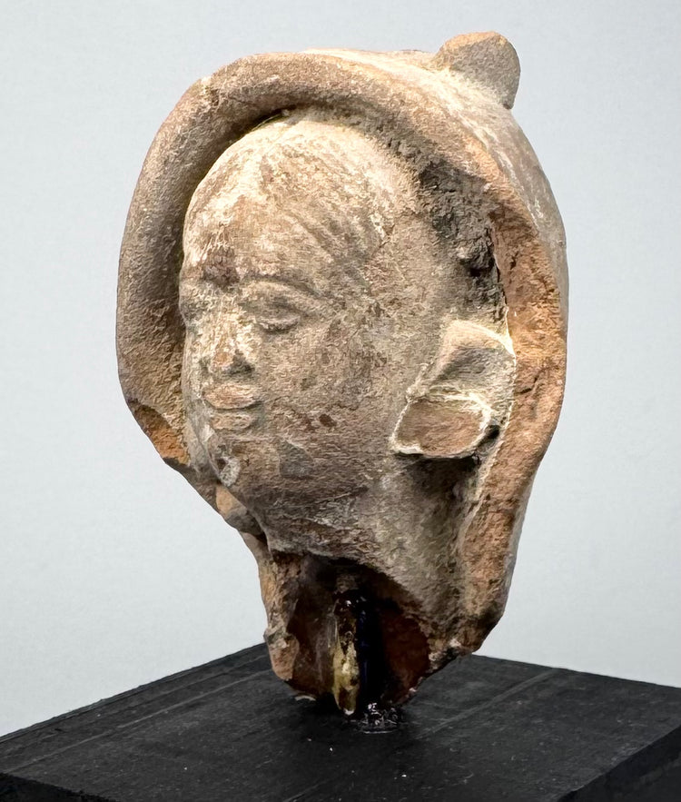 Ancient Mediterranean terracotta sculpture fragment showing a calm expression, aged patina, and partially preserved head covering.