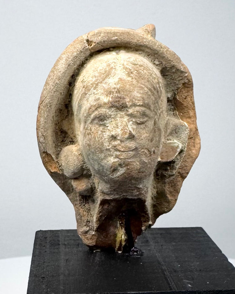 Classical antiquity terracotta head with softly modeled facial features and traces of an ancient headdress or head covering.