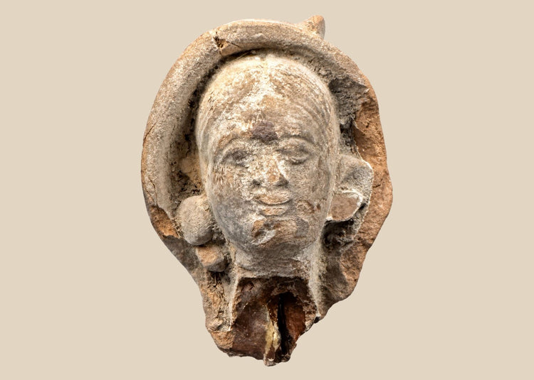 Terracotta head fragment from Classical Mediterranean, likely Greek or Roman, 1st Millennium BCE–CE. Features serene facial expression, partially preserved headdress, and natural weathered patina. Mounted on a custom stand, reflecting classical ideals of beauty, spirituality, and symbolic status in ancient art.