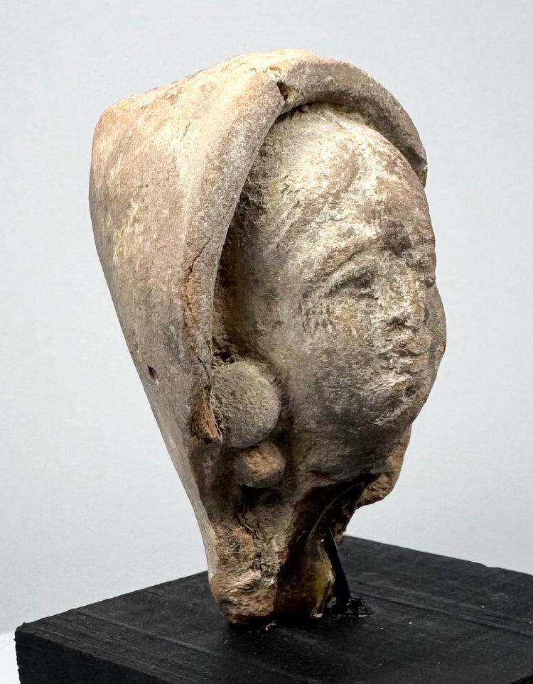 Mediterranean terracotta head from classical antiquity with weathered features, sculpted hair or head covering, and aged earthen surface.