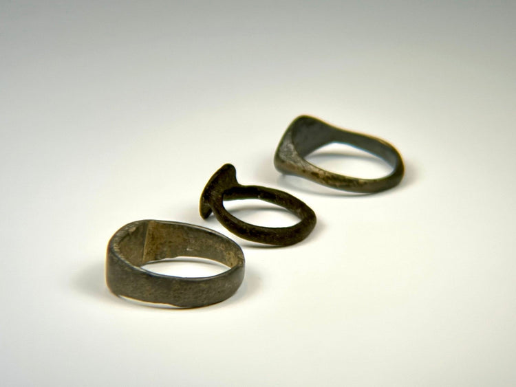 Three historic European bronze rings with engraved, shield-form, and plain band designs