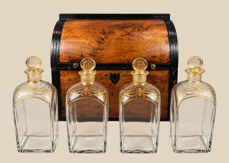 Georgian-era wooden tantalus box with red-painted interior, containing four gilded glass decanters with stoppers, used for securely storing and displaying spirits, early 19th century.