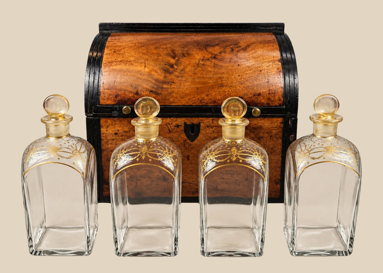 Georgian-era wooden tantalus box with red-painted interior, containing four gilded glass decanters with stoppers, used for securely storing and displaying spirits, early 19th century.