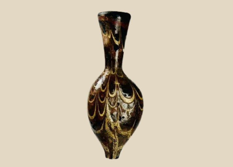 Ancient Eastern Mediterranean core-formed glass alabastron, 5th–6th Century AD, Late Roman to Byzantine period. Teardrop-shaped vessel with slender neck and pointed base, decorated with marbled browns, yellows, and gold, featuring delicate yellow trailing and swirling designs. Used for oils and perfumes, reflecting luxury, artistry, and status in antiquity.