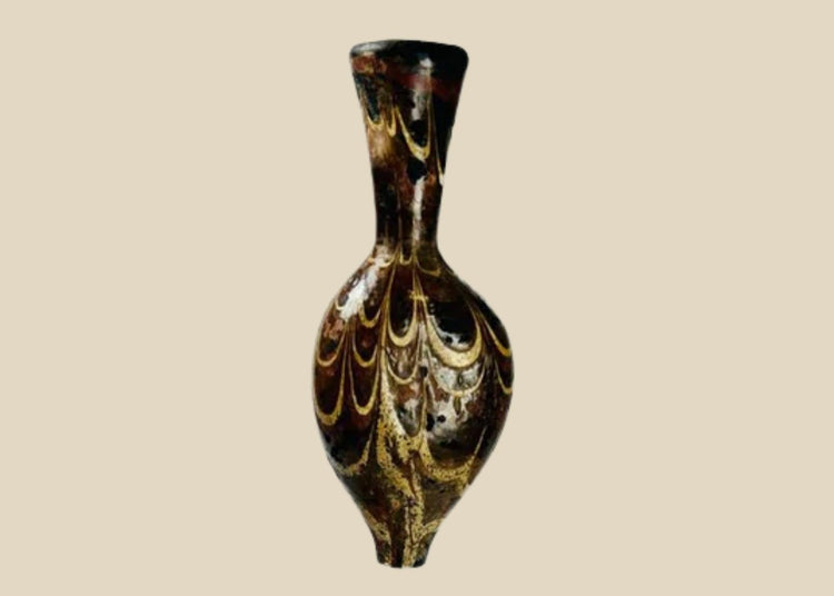 Ancient Eastern Mediterranean core-formed glass alabastron, 5th–6th Century AD, Late Roman to Byzantine period. Teardrop-shaped vessel with slender neck and pointed base, decorated with marbled browns, yellows, and gold, featuring delicate yellow trailing and swirling designs. Used for oils and perfumes, reflecting luxury, artistry, and status in antiquity.