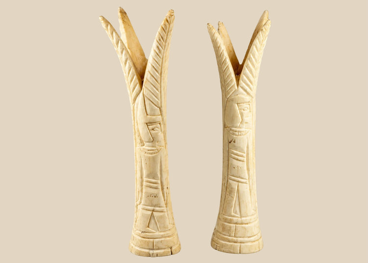 Pair of carved Egyptian ivory sistrum handles on black display bases, featuring stylized figures and decorative motifs, dating to the Third Intermediate Period, circa 1070–664 BCE.