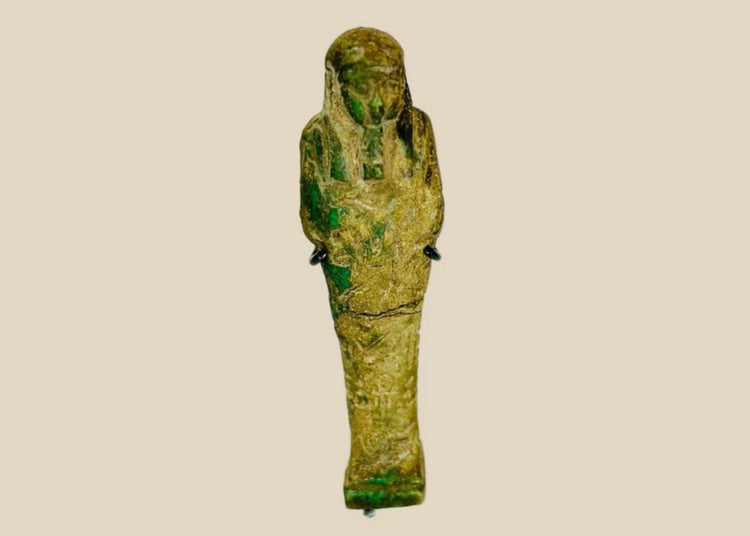 Ancient Egyptian green glazed faience Ushabti from the Late Period (664–332 BCE). Mummiform figure with tripartite wig, striated beard, and arms crossed holding hoe and pick. Hieroglyphic inscriptions adorn the body, symbolizing service in the afterlife. Reflects Egyptian funerary practices, craftsmanship, and spiritual beliefs.