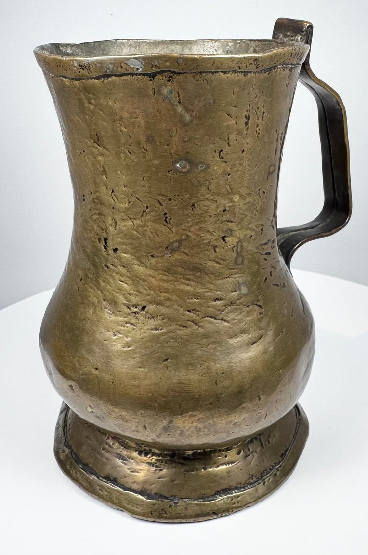 18th-century brass ale tankard displaying its curved handle, rounded body, and characteristic Georgian period construction.