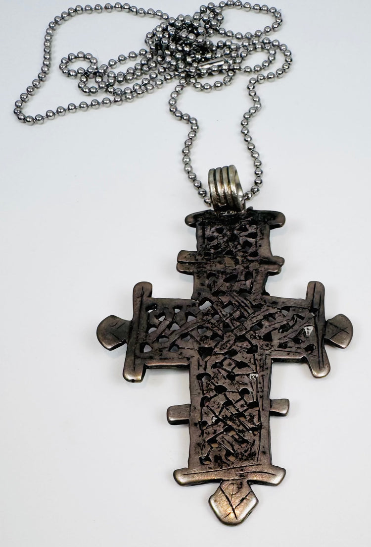 Silver-tone Ethiopian Orthodox cross pendant with ornate openwork decoration and large hanging loop.