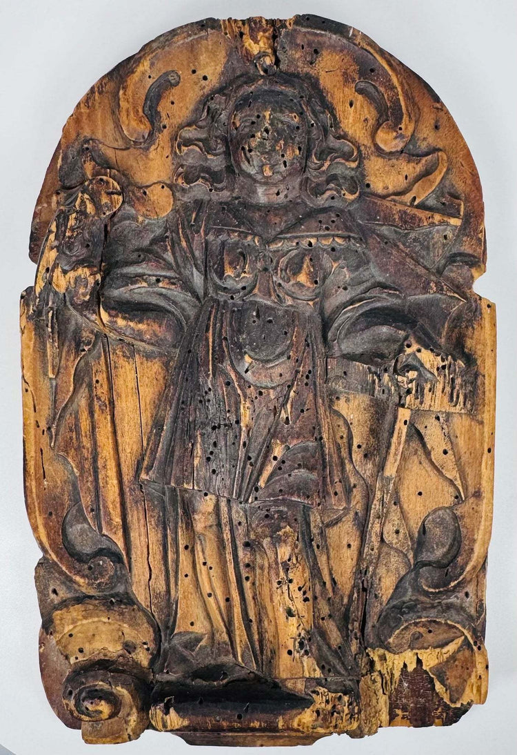 Weathered European religious wood carving with a robed saint beneath a rounded ornamental arch