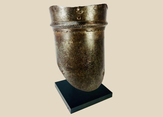 16th-century European upper arm armor, cannon-style plate with scalloped edge detailing, aged patina, and mounted on a display stand.