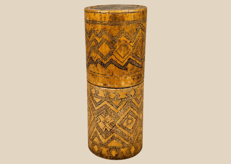 Antique carved bamboo container from Island Southeast Asia, 19th century, cylindrical with fitted lid and base, decorated with incised geometric patterns darkened with pigment, traditionally used for betel nut lime storage, photographed on a white background.
