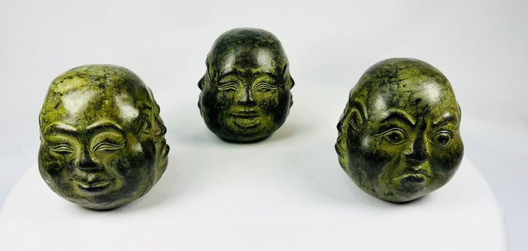 Set of three cast metal Buddhist heads with green patina in traditional brocade box