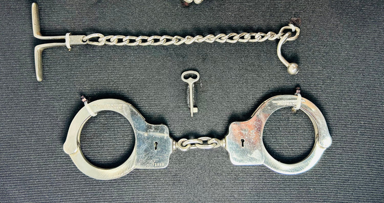 Close-up of antique 19th–20th century iron handcuffs and wrist restraints with original keys, displayed on a dark fabric background.