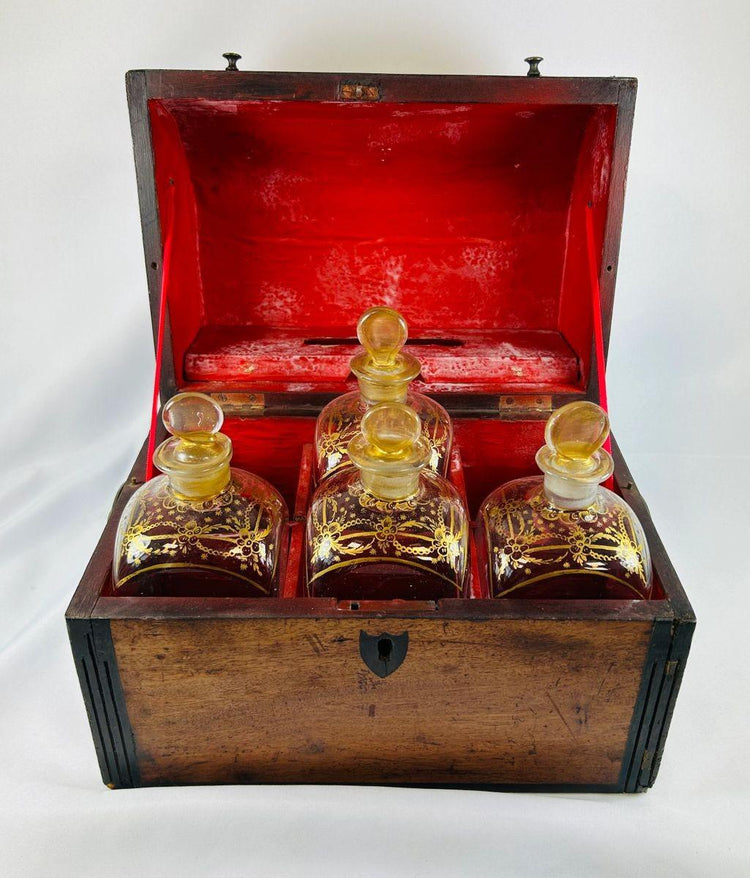 Georgian-era wooden tantalus box with red-painted interior, containing four gilded glass decanters with stoppers, used for securely storing and displaying spirits, early 19th century.