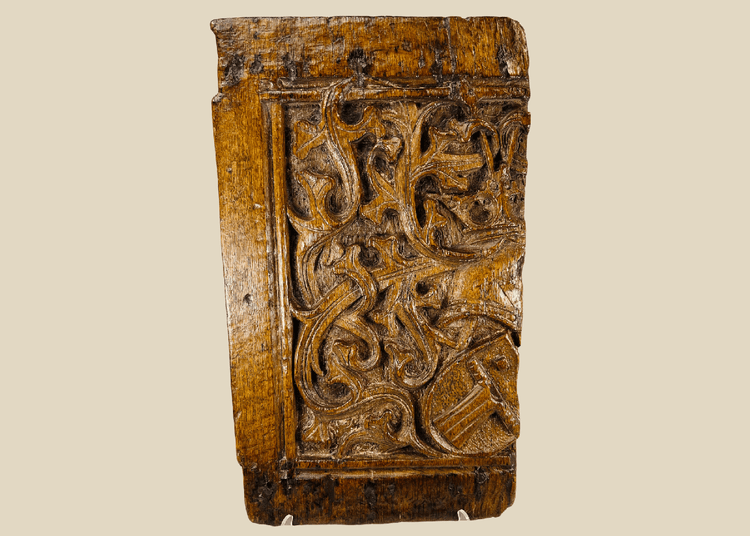 Front view of 16th-century Gothic carved oak panel showing central heraldic shield framed by foliate scrollwork.