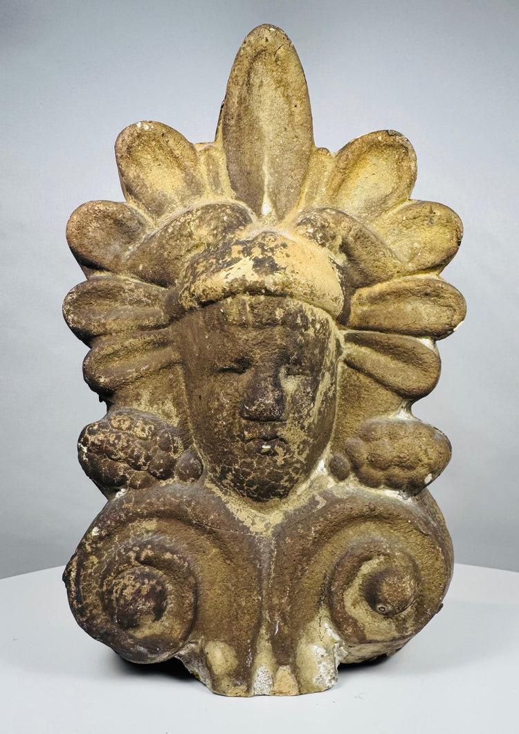Antique Greek terracotta roof ornament featuring a classical face framed by decorative volutes and a radiating palmette motif.