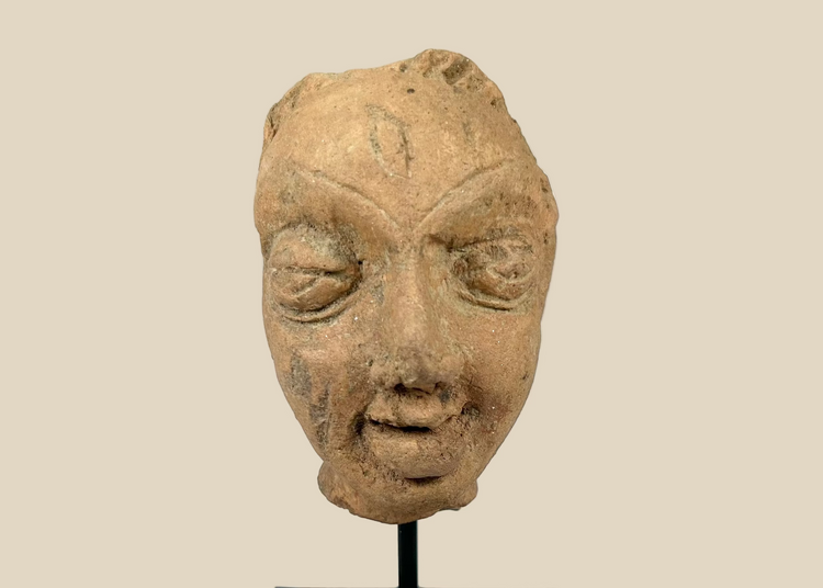 Gupta-period Northern Indian terracotta head fragment with serene almond-shaped eyes, arched brows, and softly smiling lips, warm earthen tones with mineral deposits, 3rd–5th century CE, mounted on modern display stand for preservation.