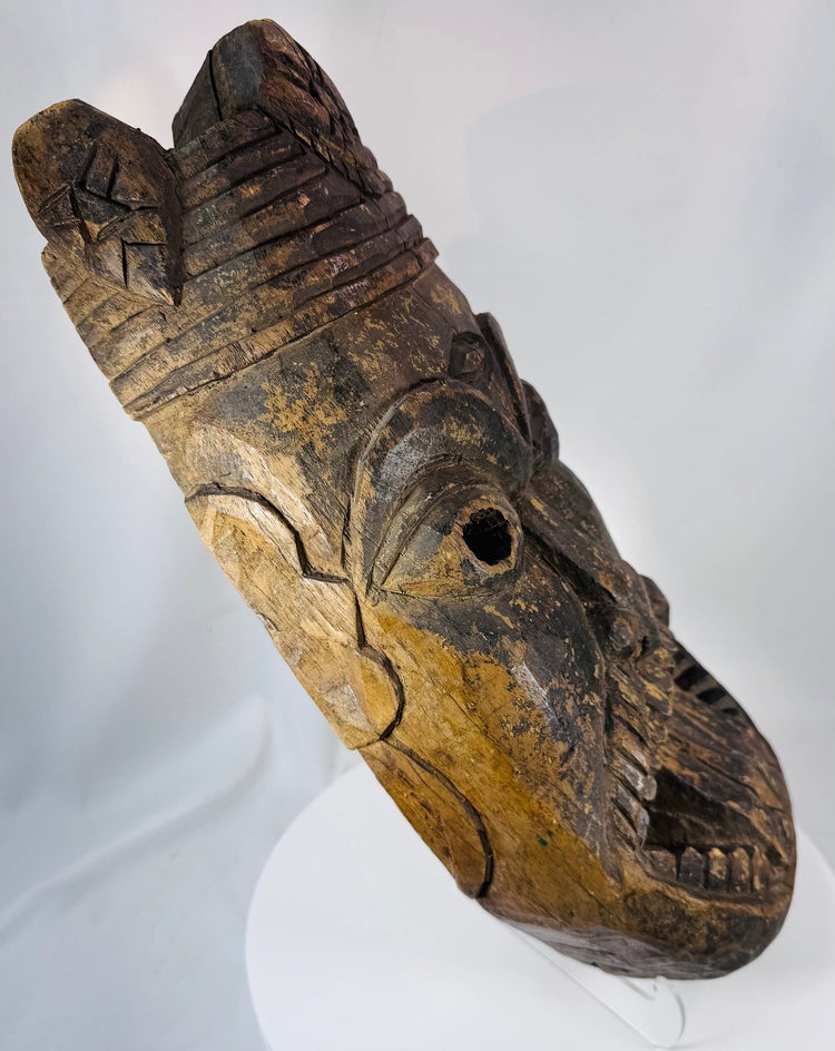 Ethnographic West African hardwood mask displaying bold spiritual imagery and weathered surface pigmentation.