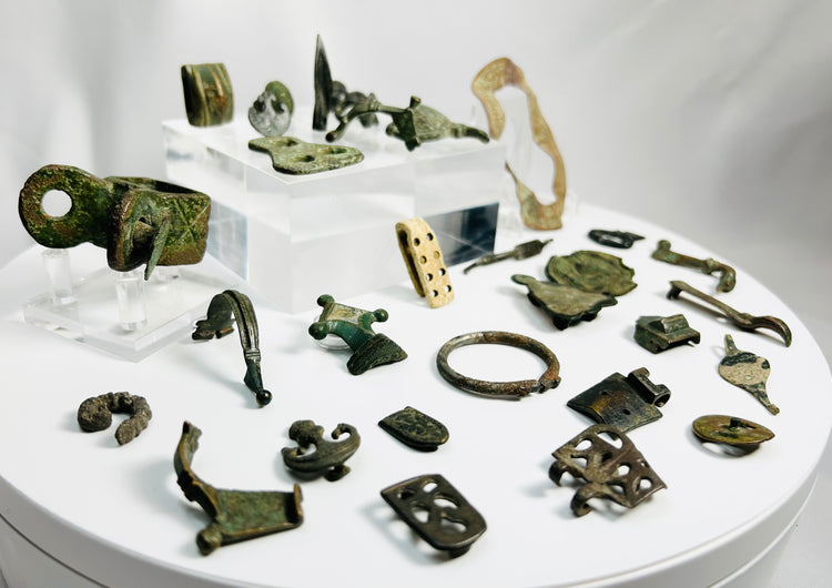 Study collection of Roman Empire bronze artifacts including buckles, strap plates, horse harness fittings, and bone gaming piece dating approximately 1,600–2,000 years old