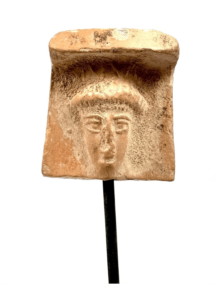 Archaic Greek terracotta female head fragment displaying a broad veil-like covering, softened facial modelling, and natural surface encrustations.