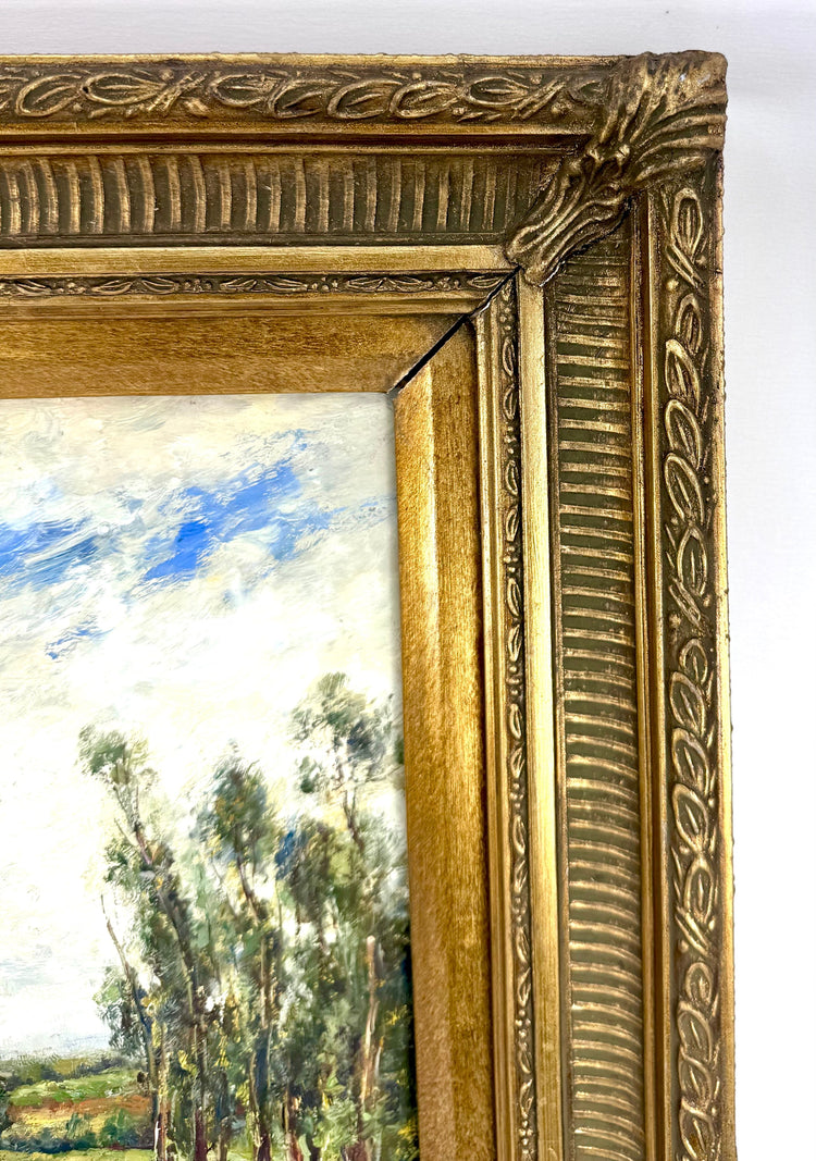 Vintage oil on canvas painting featuring tall riverside trees, rolling green fields, soft white clouds, and an expansive blue sky.