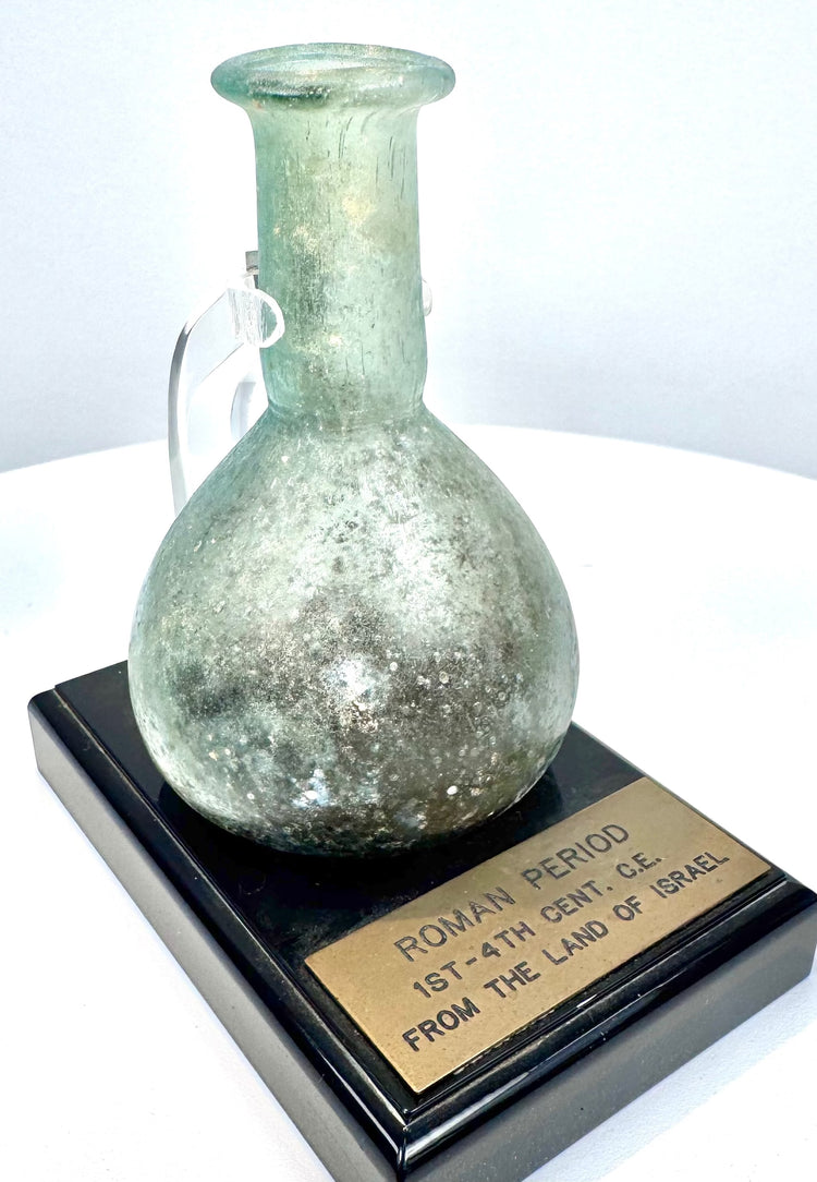 Ancient Roman free-blown glass vessel exhibiting pale turquoise coloration, earthy encrustations, and traditional early Imperial glassmaking characteristics.