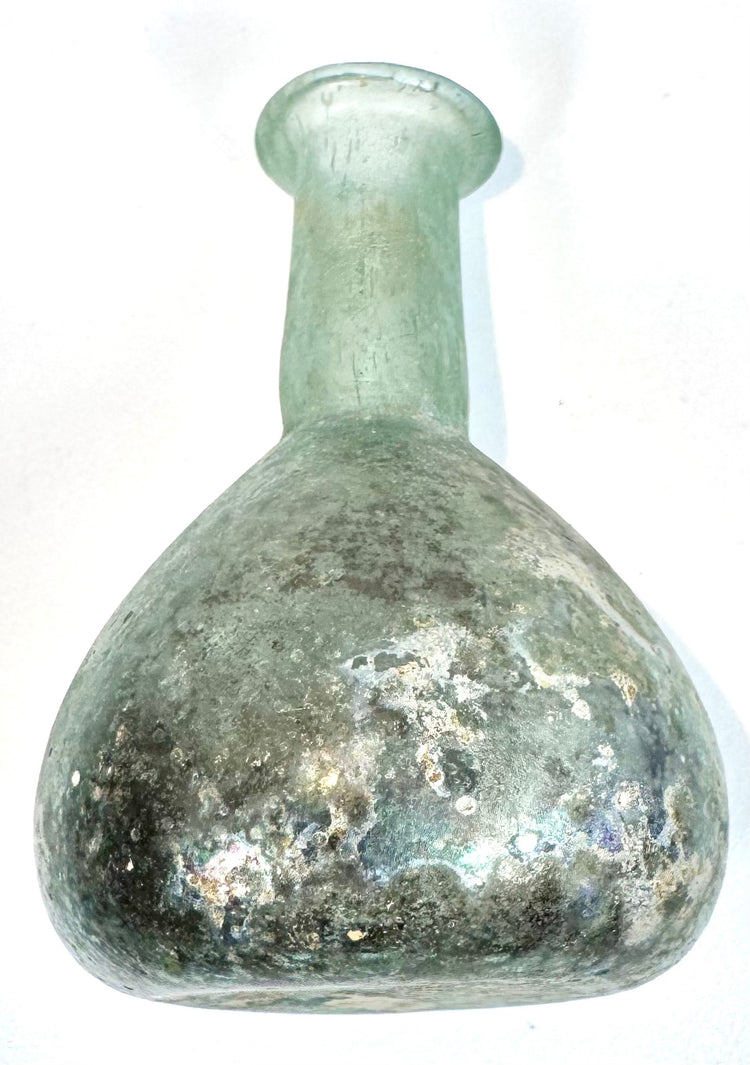 Ancient Roman glass vessel displaying concentrated mineral encrustations, dark earthy deposits, and iridescent weathering across its spherical body.