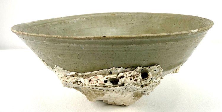 Twelfth-century Chinese celadon pottery bowl recovered from the Jepara Shipwreck, displaying marine encrustations and naturally weathered ceramic surfaces.