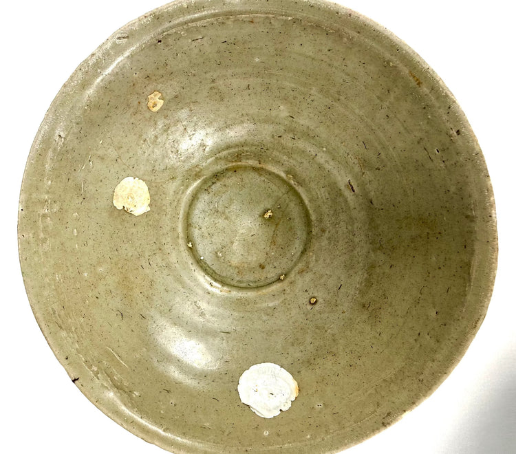 Song Dynasty celadon ceramic bowl recovered from the Jepara Shipwreck, preserving its original pale green glaze beneath areas of marine encrustation.