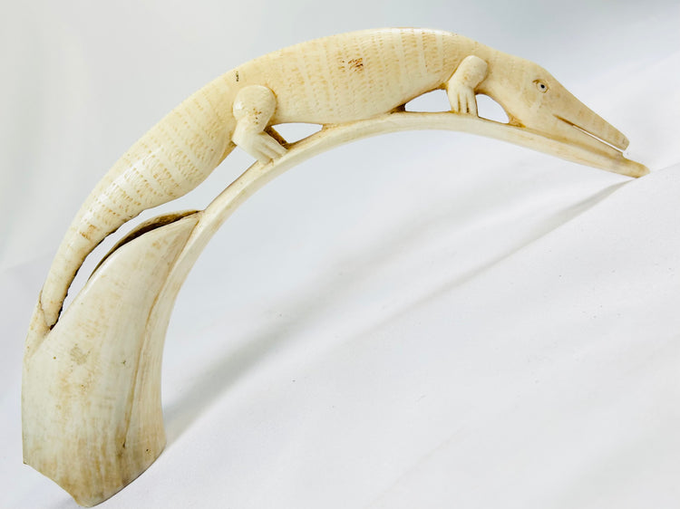 Carved African hippopotamus tooth featuring an intricately sculpted crocodile motif, early 20th-century tribal ivory artwork displayed on white background.