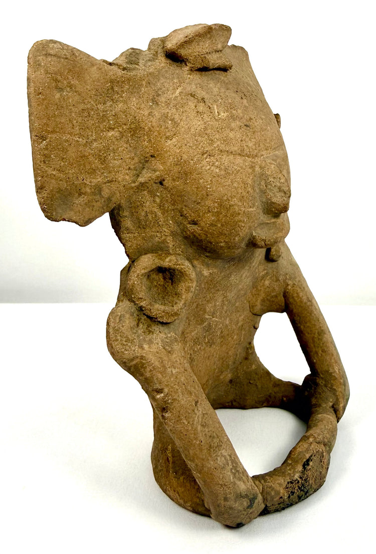 Ancient Pre-Columbian seated figure with elongated arms extending toward the lower body, earthy tan coloration, and weathered ceramic surfaces.