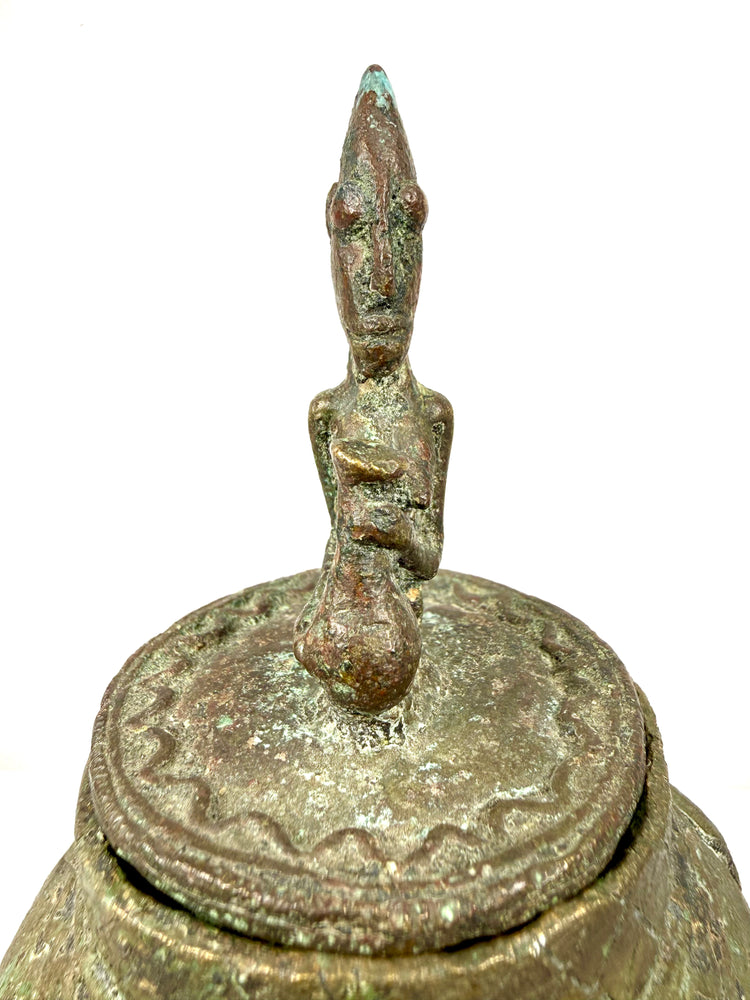 Dogon bronze container featuring a rounded body, raised ornamental detailing, and sculptural human imagery.