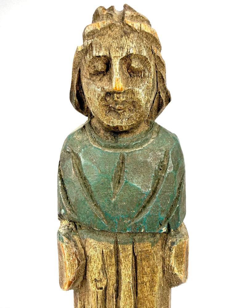 Close-up of antique European folk art wooden statue face with closed eyes and faded green paint