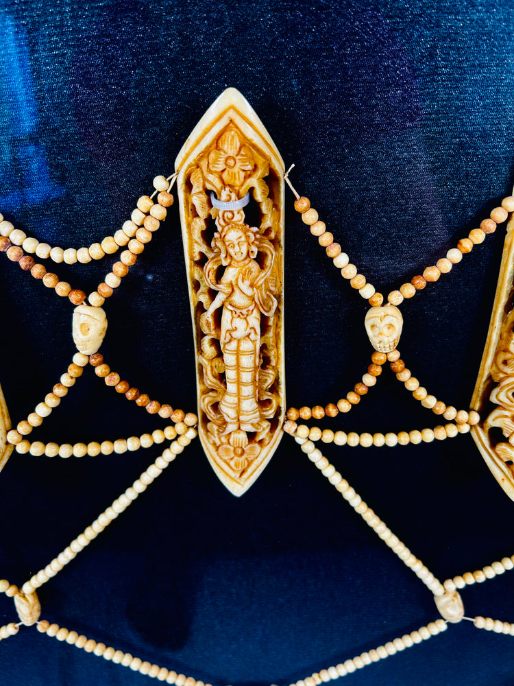 Close-up of 19th-century Tibetan Tantric ritual apron (rus gyan) plaque carved from human bone, depicting Chakrasamvara deity amid intricate beadwork on deep blue background
