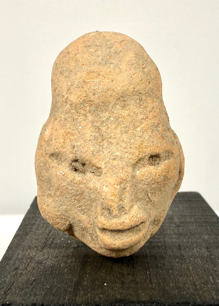 Direct frontal shot of antique terracotta head displaying symmetrical facial features on black display pedestal