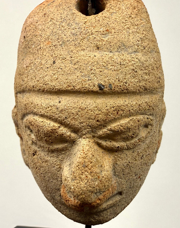 Close-up of beige terracotta amulet with sandy texture and deeply carved almond eyes