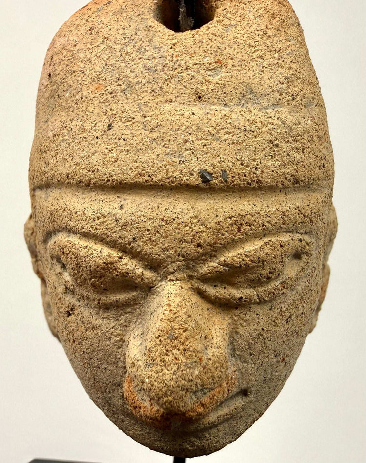 Close-up of beige terracotta amulet with sandy texture and deeply carved almond eyes